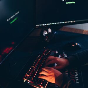 High angle of crop anonymous hacker stealing information from desktop computers with data on screens in twilight
